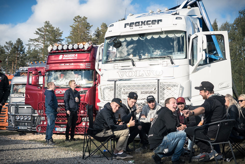 Personer sitter på tältstolar framför en vit och en röd lastbil.